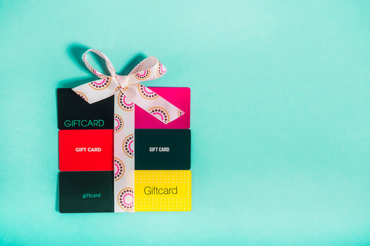 Top view colourful Shop gift cards in shape of present box with a bow of satin ribbon on bright turquoise background. Creative ideas for presents. Flat lay. Holiday sales mockup with copy space.