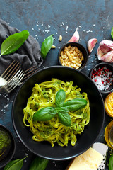 Pasta tagliatelle with pesto sauce and fresh basil leaves in black bowl. Top view with copy space.