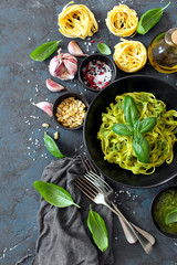 Pasta tagliatelle with pesto sauce and fresh basil leaves in black bowl. Top view with copy space.