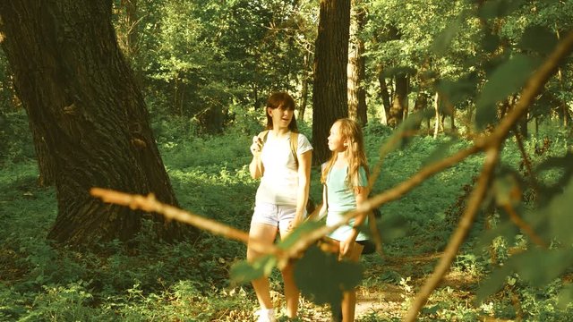 girls travelers with backpacks run through the thickest in the forest. Hiker woman walks in forest. happy hiker girl in summer park. teenager girl adventures on vacation.