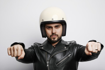 Naklejka premium Portrait of young biker in a leather jacket pretending to ride a motorcycle isolated on a white background. Horizontal.