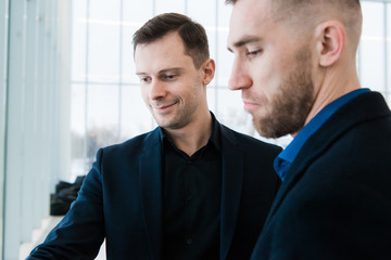 Two handsome smiling businessmen in airport, discussing important project and looking at phone screen.