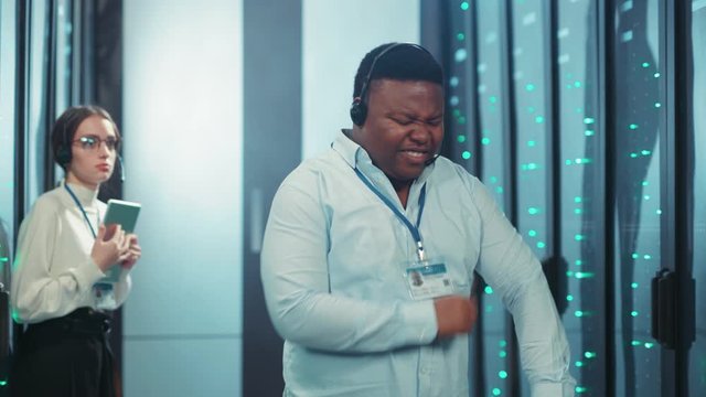 Aggressive black data center specialist arguing throwing notepad in anger. Mixed-up furious IT engineer shouting getting mad in rack server corridor at cyber security.