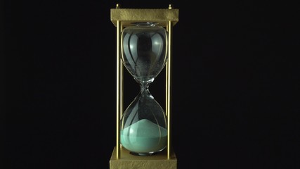 Still hourglass clock time concept. Old vintage gold metal frame green sand clock countdown on dark...