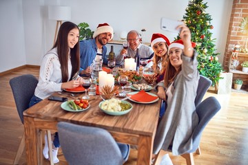 Beautiful family wearing santa claus hat meeting smiling happy and confident. Eating roasted turkey make selfie by smartphone celebrating Christmas at home