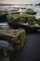 Bali island landscape sunset seaside view. Rock with seawead and black sand in long exposure