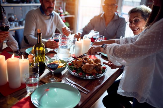 Family and friends dining at home celebrating christmas eve with traditional food and decoration, preparing turkey for dinner