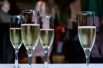 Selective focus of crystal glasses of alcoholic beverages standing on a served table with a group of people in the background
