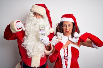 Senior couple wearing Santa Claus costume holding dollars over isolated white background Pointing down looking sad and upset, indicating direction with fingers, unhappy and depressed.