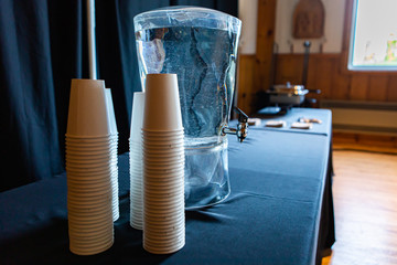 Selective focus of tank filled with water and paper cups next to it standing on a grand table with...