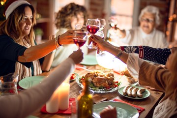 Beautiful group of women smiling happy and confident. Eating roasted turkey and toasting with cup of wine celebrating christmas at home