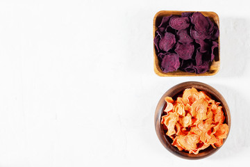 Dried carrot and beet chips in a wooden bowl on a white concrete background. Organic natural food.
