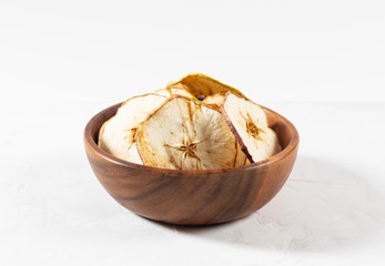 Dried apple chips in a wooden bowl on a white concrete background. Natural organic food.