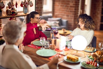Beautiful group of women smiling happy and confident. Eating roasted turkey and serving wine on cup celebrating christmas at home