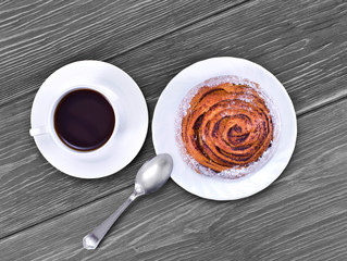 Cup of coffee and bun with cinnamon on a wooden table. Top view.