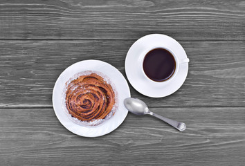 Cup of coffee and bun with cinnamon on a old wooden table. Top view.