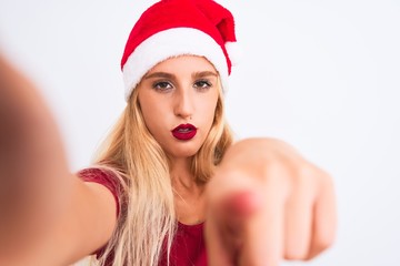 Woman wearing Christmas Santa hat make selfie by camera over isolated white background pointing with finger to the camera and to you, hand sign, positive and confident gesture from the front