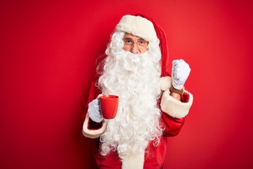 Senior man wearing Santa Claus costume holding cup of coffee over isolated red background screaming proud and celebrating victory and success very excited, cheering emotion