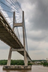 Ho Chi Minh City, Vietnam - March 12, 2019: Song Sai Gon river. One H-shaped pylon of Phu My suspension bridge is an art work of cables and concrete under gray cloudscape. Brown water.
