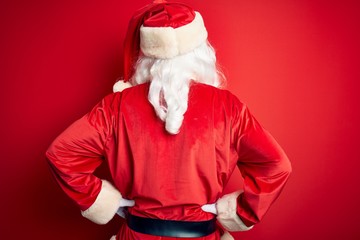 Middle age handsome man wearing Santa costume standing over isolated red background standing backwards looking away with arms on body