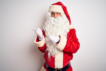 Middle age handsome man wearing Santa costume standing over isolated white background Pointing to the back behind with hand and thumbs up, smiling confident