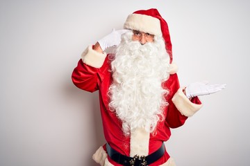 Middle age handsome man wearing Santa costume standing over isolated white background confused and annoyed with open palm showing copy space and pointing finger to forehead. Think about it.
