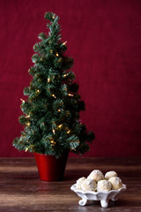 White dish with Russian Tea Cake cookies, artificial Christmas tree with white lights, wood table, red background