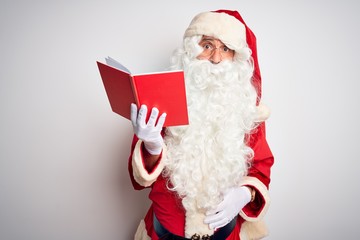 Middle age man wearing Santa Claus costume reading book over isolated white background In shock...