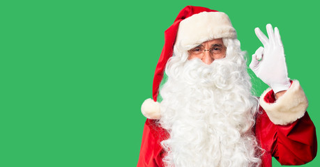 Middle age handsome man wearing Santa Claus costume and beard standing smiling positive doing ok sign with hand and fingers. Successful expression.