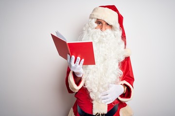 Naklejka premium Middle age man wearing Santa Claus costume reading book over isolated white background Relaxed with serious expression on face. Simple and natural looking at the camera.