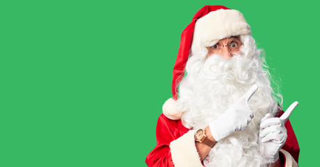 Middle age handsome man wearing Santa Claus costume and beard standing Pointing aside worried and nervous with both hands, concerned and surprised expression