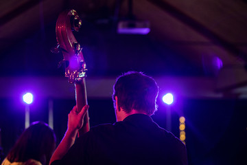 Backside view of adult male giving a live performance on stage by playing songs on a bowing instrument 