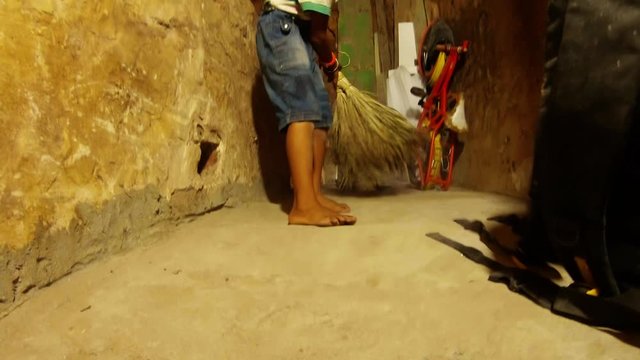 little indian boy sweeps with broom shabby room bicycle and boards in corner slum of Varanasi