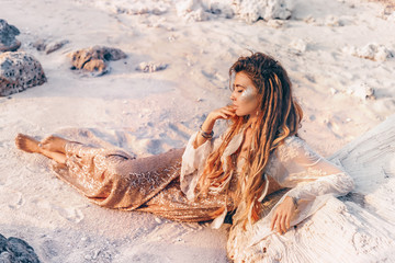 beautiful young woman in elegant dress lying on sand at the beach at sunset
