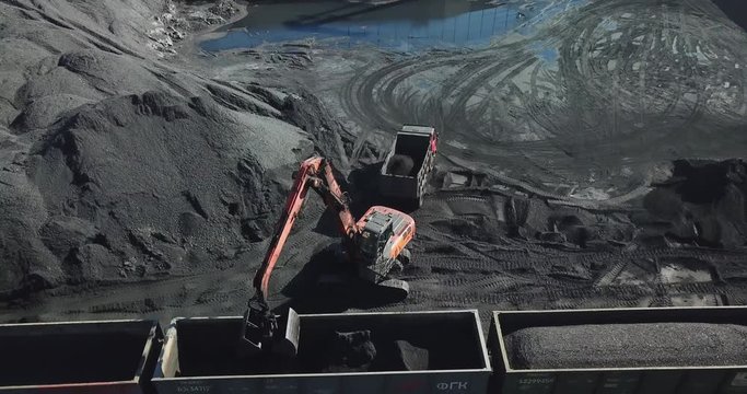 Coal port top view. Loading coal into railway wagons using an excavator. Stevedoring company.