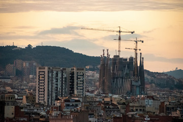 Obraz premium A view of the still under construction Sagrada Familia with its construction cranes during sunset with mountains in the background
