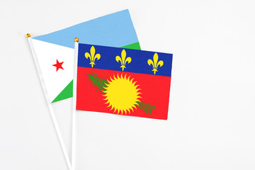 Guadeloupe and Djibouti stick flags on white background. High quality fabric, miniature national flag. Peaceful global concept.White floor for copy space.