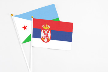 Serbia and Djibouti stick flags on white background. High quality fabric, miniature national flag. Peaceful global concept.White floor for copy space.