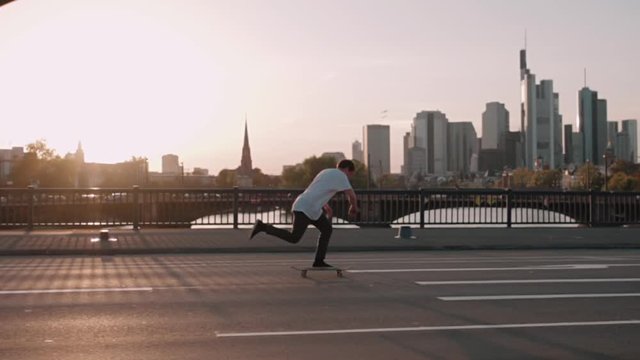 skateboarder pushing on bridge in super slow motion in front frankfurt skyline skyscrapers sunset