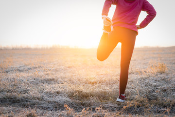 Adult fitness sportswoman runner stretching legs before run on field.