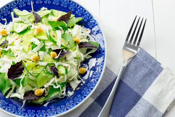 Green salad with sprouted chickpeas in a blue plate on a light background. Vegetarian raw food.