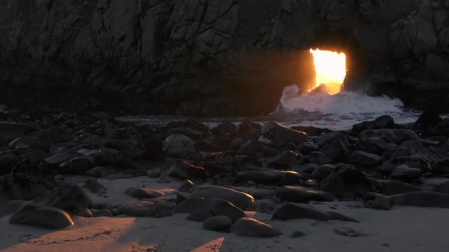 Magical sunlight cuts through a keyhole archway in the sea rock as beautiful Pfeiffer Beach at Big Sur California. The sun aligning with this natural ocean corridor only happens once a year. 