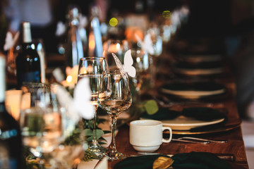 Banquet or holiday background in a rustic atmosphere. Dinner table setting. Vintage decoration of reception table. Elegant arrangement of the holiday tableware. Wine glasses, plates, forks.