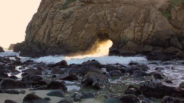 Awesome keyhole rock allows the splashing surf to cut through the unique rock formations at Pfeiffer Beach in Western California dressed in orange and teal natural complimentary colors. 