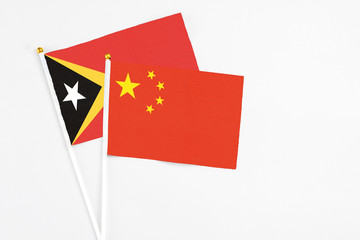 China and East Timor stick flags on white background. High quality fabric, miniature national flag. Peaceful global concept.White floor for copy space.