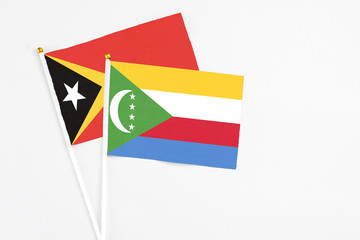 Comoros and East Timor stick flags on white background. High quality fabric, miniature national flag. Peaceful global concept.White floor for copy space.