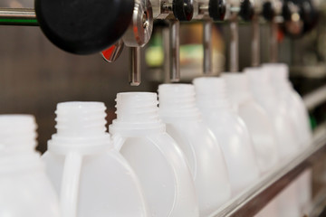 white plastic gallons or bottles on the production line of the conveyor at filling machine in the...