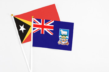 Fototapeta premium Falkland Islands and East Timor stick flags on white background. High quality fabric, miniature national flag. Peaceful global concept.White floor for copy space.