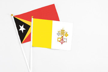 Vatican City and East Timor stick flags on white background. High quality fabric, miniature national flag. Peaceful global concept.White floor for copy space.
