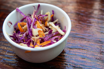 Vegan coleslaw in white bowl on wooden table. Mixed sliced vegetables. Vegetarian side dish.